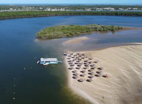 Vista aérea da Croa do Goré: o banco de areia emergindo do rio, com fileiras de guarda-sóis de palha e o catamarã ancorado ao lado